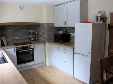 A kitchen with white cabinets a built in oven a microwave a fridge and wooden countertops at Tuckermarsh Quay River Cottage 2 Bere Alston near Tavistock