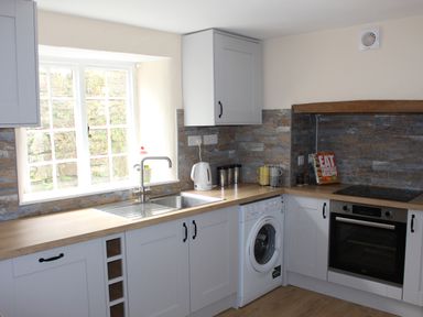 A kitchen with white cabinets a sink a washing machine an oven and a kettle at Tuckermarsh Quay River Cottage 2 Bere Alston near Tavistock