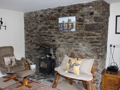 A room with a stone fireplace wood burning stove armchair with ottoman and wooden bench with cushions at Tuckermarsh Quay River Cottage 2 Bere Alston near Tavistock