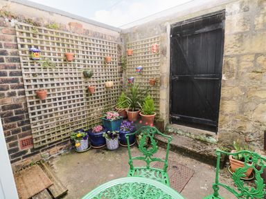 An outdoor patio with green metal table and chairs potted plants on lattice against brick wall and black wooden door at Coquet Cottage in Amble
