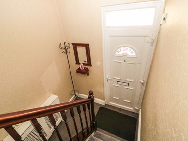 A stairway and front door area with a coat stand, small wall mirror, and a black floor mat at Coquet Cottage in Amble