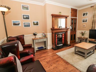 A living room with leather armchairs a fireplace a coffee table and framed pictures on the walls at Coquet Cottage in Amble