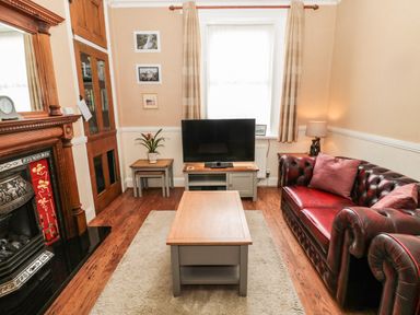 A living room with a leather sofa a coffee table a television and a fireplace at Coquet Cottage in Amble