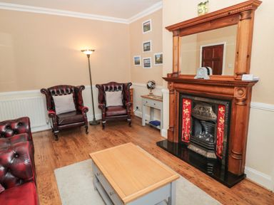 A living room with leather armchairs a wooden fireplace and a coffee table at Coquet Cottage in Amble