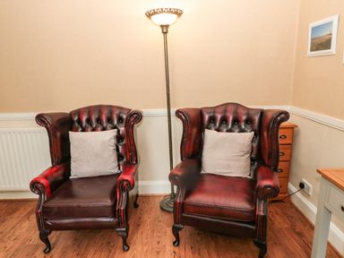 Two leather armchairs with cushions next to a floor lamp in a room with wooden floor at Coquet Cottage in Amble