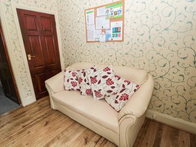 A beige sofa with red and white floral cushions next to a closed wooden door and a bulletin board on floral wallpaper at Coquet Cottage in Amble