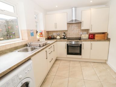 A kitchen with white cabinets a stainless steel oven a tiled backsplash and a washing machine under the counter at Coquet Cottage in Amble