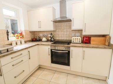 A kitchen with white cabinets stove oven toaster and window at Coquet Cottage in Amble