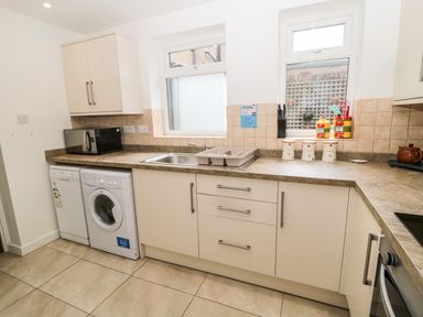 A kitchen with a washing machine microwave sink and containers on the counter at Coquet Cottage in Amble