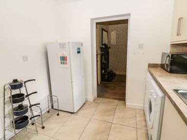 A kitchen with a white fridge, pot rack, washing machine, microwave, and brown countertop at Coquet Cottage in Amble