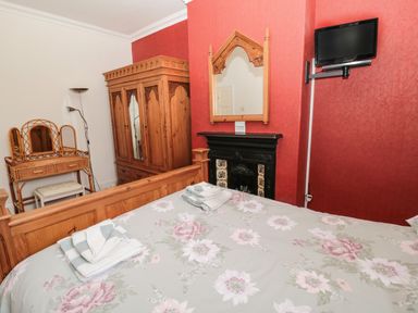 A bedroom with a wooden bed with floral bedding wooden wardrobe dressing table and a wall-mounted television at Coquet Cottage in Amble