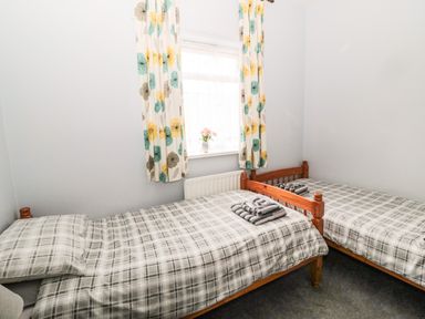 A bedroom with two single beds with plaid bedding and colorful floral curtains at Coquet Cottage in Amble