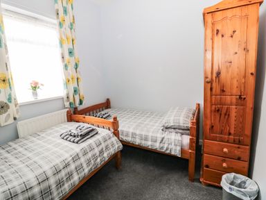 A bedroom with two single beds a wooden wardrobe and a window with patterned curtains at Coquet Cottage in Amble