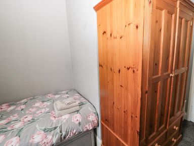 A bedroom corner with a single bed with floral bedding and folded towels next to a wooden wardrobe at Coquet Cottage in Amble