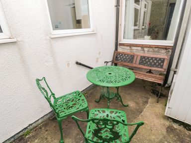 Small outdoor seating area with green metal table, two green metal chairs, and wooden bench against white walls at Coquet Cottage in Amble