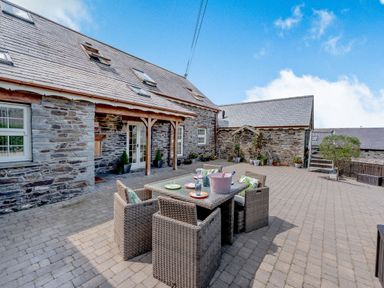 A patio with a dining table and chairs outside a stone building at Ysgubor Uchaf in Brongest near Newcastle Emlyn