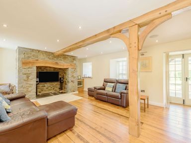 A living room with leather sofas a stone fireplace wooden beams and hardwood floor at Ysgubor Uchaf in Brongest near Newcastle Emlyn