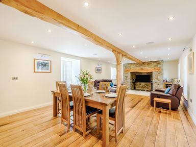 A dining area with a wooden table and chairs next to a living room with leather sofas and a stone fireplace at Ysgubor Uchaf in Brongest near Newcastle Emlyn