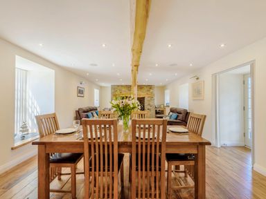 A dining room with a wooden table and six chairs a flower vase on the table and two brown leather sofas in the background at Ysgubor Uchaf Brongest near Newcastle Emlyn