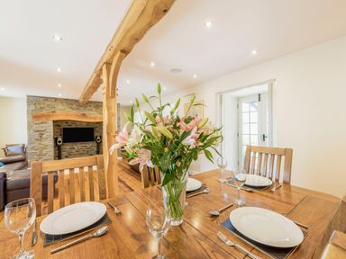 A dining table set with plates glasses and cutlery and a vase of flowers in a room with exposed wooden beams and a stone fireplace at Ysgubor Uchaf in Brongest near Newcastle Emlyn