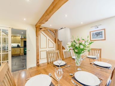 A dining room with wooden table and chairs set with plates and glasses and flowers in a vase at Ysgubor Uchaf in Brongest near Newcastle Emlyn