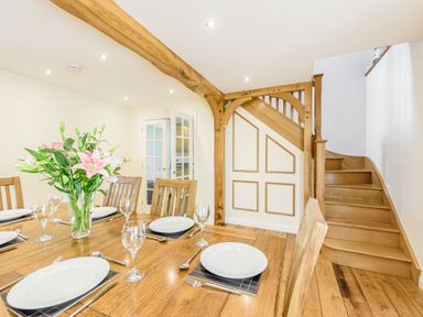 A dining room with a wooden table set with white plates glassware and cutlery with a flower arrangement and wooden stairs in the background at Ysgubor Uchaf Brongest near Newcastle Emlyn