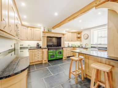 A kitchen with wooden cabinets a green oven and two wooden stools at Ysgubor Uchaf Brongest near Newcastle Emlyn