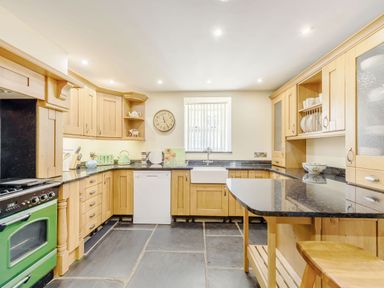 A kitchen with wooden cabinets black countertops a green oven dishwasher and a window with blinds at Ysgubor Uchaf in Brongest near Newcastle Emlyn