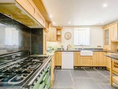 A kitchen with wooden cabinets a gas stove a dishwasher a sink and a clock on the wall at Ysgubor Uchaf in Brongest near Newcastle Emlyn