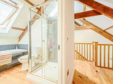 A bathroom with a bathtub toilet and shower next to a wooden staircase and exposed beams at Ysgubor Uchaf Brongest near Newcastle Emlyn
