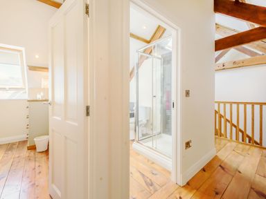 A hallway with wooden floors leading to a bathroom with a glass shower enclosure and a toilet at Ysgubor Uchaf Brongest near Newcastle Emlyn