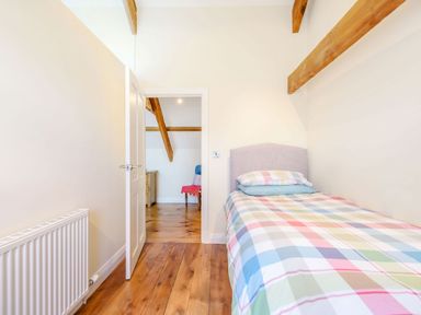 A bedroom with a single bed with checkered bedding wooden floor and exposed wooden beams at Ysgubor Uchaf in Brongest near Newcastle Emlyn