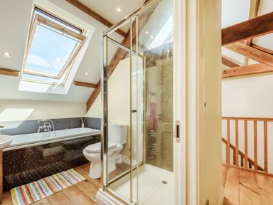 A bathroom with a bathtub under a skylight window a toilet and a glass shower enclosure with wooden beams on the ceiling at Ysgubor Uchaf in Brongest near Newcastle Emlyn