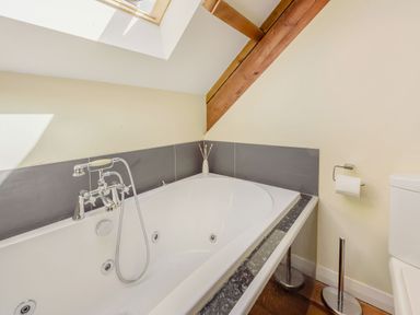 A bathroom with a bathtub a toilet a skylight and wooden beams at Ysgubor Uchaf in Brongest near Newcastle Emlyn