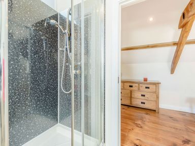 A shower with a glass door and black speckled wall next to a wooden dresser on a wooden floor at Ysgubor Uchaf in Brongest near Newcastle Emlyn