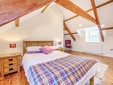 A bedroom with wooden beams a bed bedside tables lamps a chair and a window at Ysgubor Uchaf in Brongest near Newcastle Emlyn