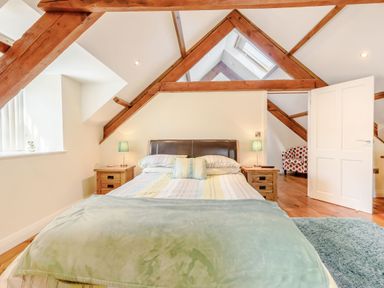 A bedroom with a bed two bedside tables with lamps exposed wooden beams and an armchair at Ysgubor Uchaf in Brongest near Newcastle Emlyn