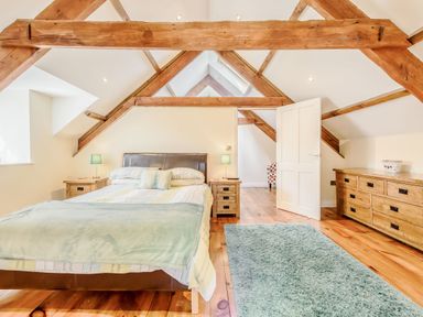 A bedroom with a double bed wooden nightstands a dresser and exposed wooden ceiling beams at Ysgubor Uchaf in Brongest near Newcastle Emlyn