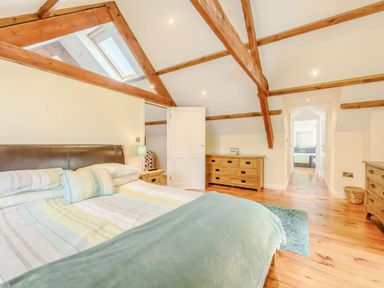 A bedroom with wooden beams a double bed wooden dressers and a skylight at Ysgubor Uchaf in Brongest near Newcastle Emlyn