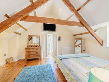A bedroom with wooden beams a dresser a floor mirror a bed with striped bedding and a blue rug at Ysgubor Uchaf in Brongest near Newcastle Emlyn