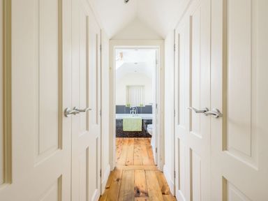 A hallway with wooden floors and white doors leading to a bathroom with a bathtub and green towel at Ysgubor Uchaf Brongest near Newcastle Emlyn