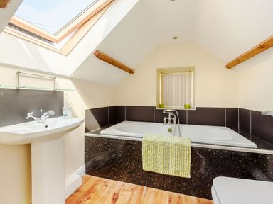 A bathroom with a bathtub sink skylight and wooden floor at Ysgubor Uchaf in Brongest near Newcastle Emlyn