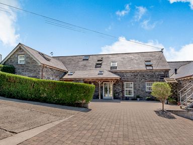 A stone house with multiple windows and skylights surrounded by hedges and paved driveway at Ysgubor Uchaf in Brongest near Newcastle Emlyn