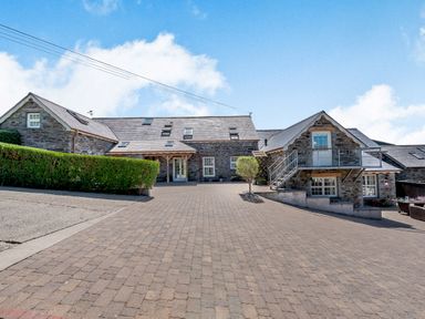 A stone house with multiple windows and a balcony over a paved driveway at Ysgubor Uchaf in Brongest near Newcastle Emlyn
