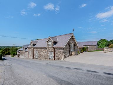 A stone building with multiple windows and a slate roof beside a paved road at Ysgubor Uchaf in Brongest near Newcastle Emlyn