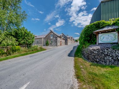 A road leading to stone buildings with a green metal structure and a sign on the right and trees on the left at Ysgubor Uchaf in Brongest near Newcastle Emlyn