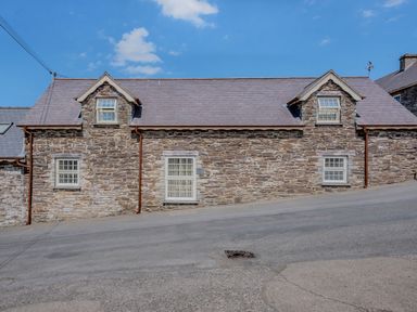 A stone cottage with windows and a sloped roof next to a paved road at Ysgubor Uchaf in Brongest near Newcastle Emlyn