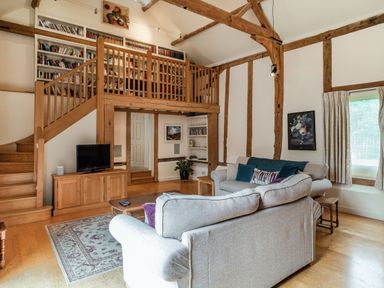A living room with wooden beams bookshelves a TV on a cabinet sofas a coffee table and a staircase at Ducksfoot Barn Bush Green near Pulham Market