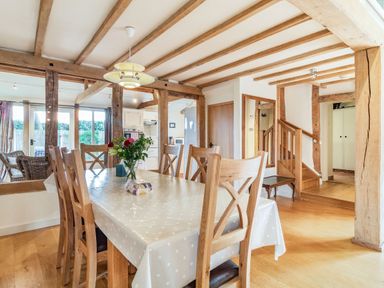 A dining room with a wooden table and chairs and a vase of flowers at Ducksfoot Barn Bush Green near Pulham Market