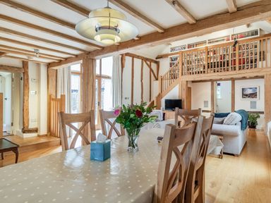 A dining area with a table and chairs and a living room with sofas and a staircase in a rustic house at Ducksfoot Barn in Bush Green near Pulham Market